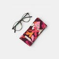 Funda de gafas estampada floral tuá e muá con cierre a presión y gafas de vista negras al lado.