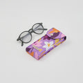 Funda de lona impermeable morada con estampado floral para gafas, interior de algodón suave, cierre de broche. Marca tuá e muá.