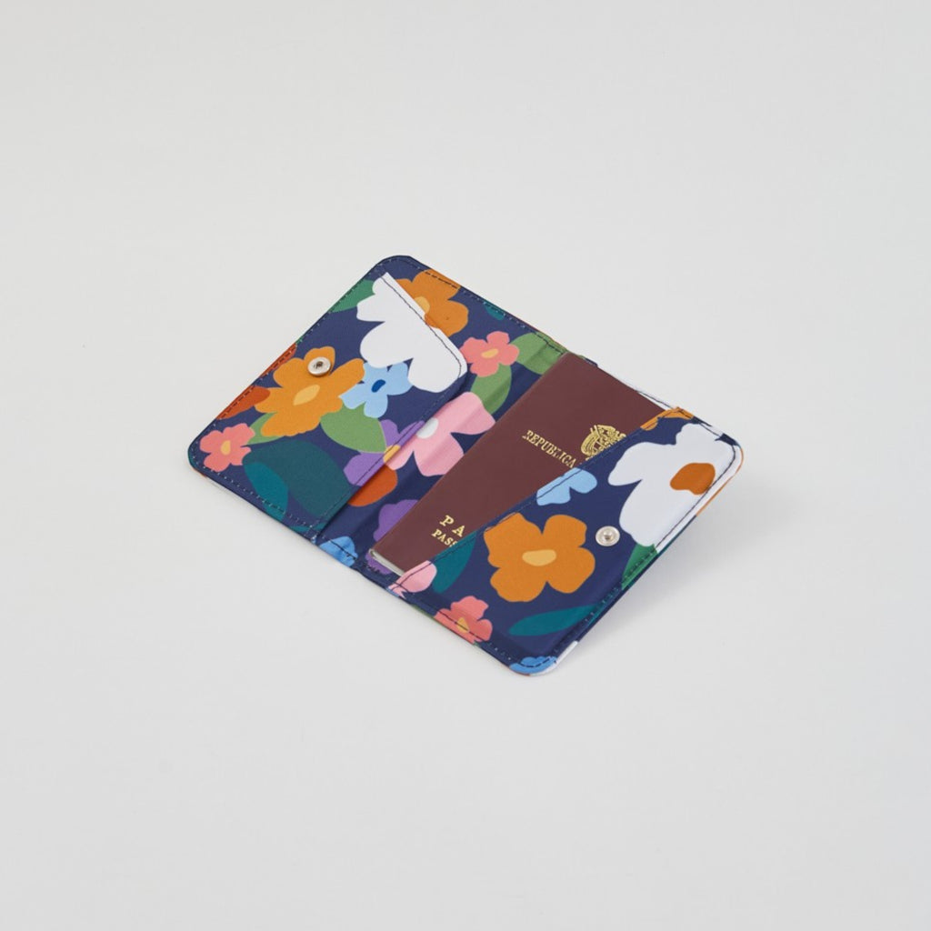 tuá e muá Porta Pasaporte Flora con estampado floral multicolor sobre fondo azul marino, fabricado en lona impermeable.